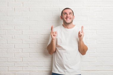 Beyaz delikanlı geçiş parmakları umut ve gözler gülümseyen beyaz tuğla duvarın üzerinden ayakta kapalı. Şans ve batıl kavramı.