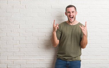 Deli ifade rock simge elle yapıyor ile bağırarak beyaz tuğla duvarın üzerinden ayakta beyaz delikanlı. Müzik yıldızı. Ağır kavramı.