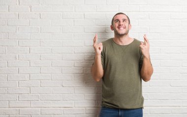 Beyaz delikanlı geçiş parmakları umut ve gözler gülümseyen beyaz tuğla duvarın üzerinden ayakta kapalı. Şans ve batıl kavramı.