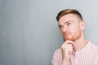 Gri grunge duvar ciddi bir yüz düşünme hakkında soru, çok karışık fikir genç Kızıl saçlı adam