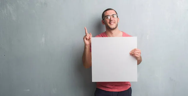 Young Caucasian Man Grey Grunge Wall Holding Blank Banner Surprised — Stock Photo, Image