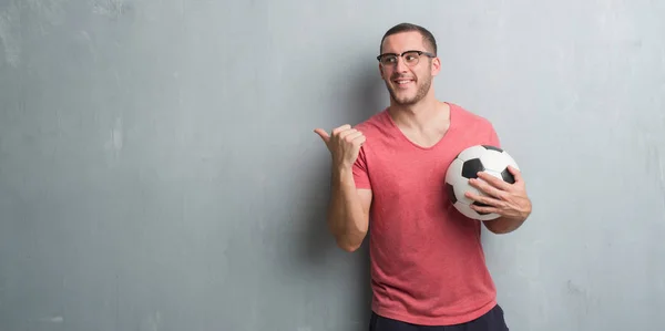 Jovem Caucasiano Sobre Parede Grunge Cinza Segurando Bola Futebol Apontando — Fotografia de Stock