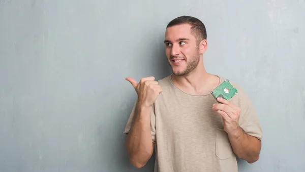 Joven Hombre Caucásico Sobre Pared Grunge Gris Sosteniendo Disco Duro — Foto de Stock