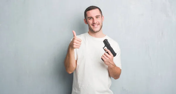 Jonge Kaukasische Criminele Man Grijs Grunge Muur Gun Gelukkig Houden — Stockfoto
