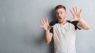 Şokta bağırarak gri grunge duvar korkuyor ve dehşet korku ifade dur hareketi el ile ile genç Kızıl saçlı adam. Panik kavramı.