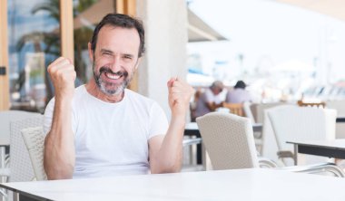 Duygu tezahürat yakışıklı üst düzey adam gurur çığlık ve zafer ve başarı çok heyecanlı, kutluyor Terrace'da oturuyor