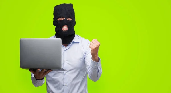 Business hacker man holding a computer laptop screaming proud and celebrating victory and success very excited, cheering emotion