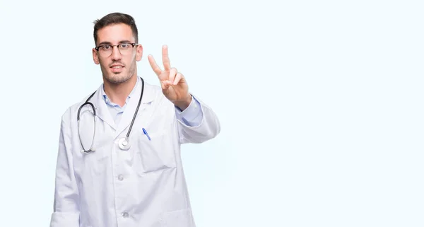 勝利のサインをやって指を表示するカメラを笑みを浮かべてハンサムな若い医者の男 — ストック写真