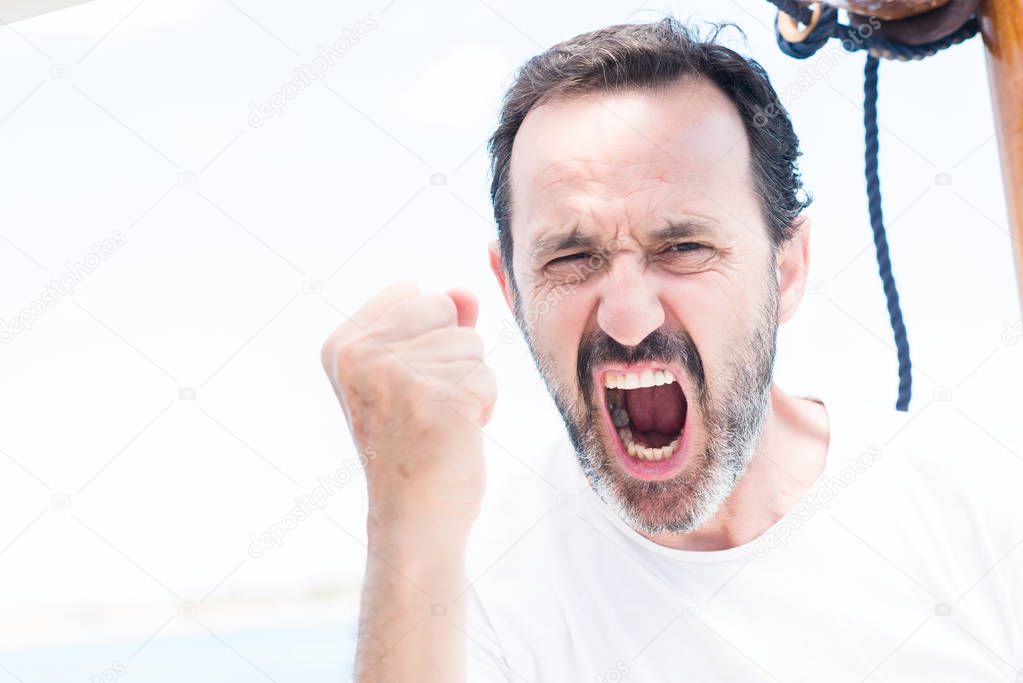 Handsome senior man traveling on sailboat annoyed and frustrated shouting with anger, crazy and yelling with raised hand, anger concept