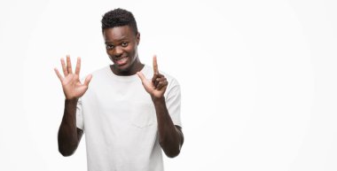 Gösterilen ve parmakları ile işaret beyaz t-shirt giyen genç Afro-Amerikan adam kendinden emin ve mutlu gülümseyerek süre yedi numara.
