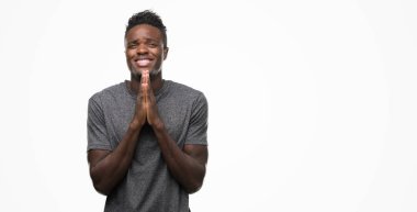 Birlikte AF emin gülümseyen için soran ile dua gri t-shirt giyen genç Afro-Amerikan adam eller.