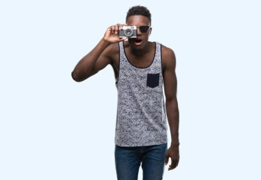 Genç Afro-Amerikan adam holding vintage kamera bir sürpriz yüz, korkuyor ve heyecanlı korku ifadesi ile şok korkmuş