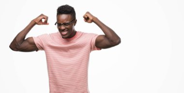 Pembe tişört gösteren kol kasları gururlu gülümseyen giyen genç Afro-Amerikan adam. Fitness kavramı.
