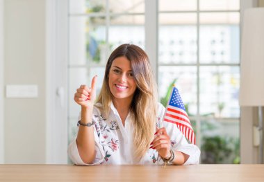 Genç kadın evde Amerika Birleşik Devletleri bayrağı ok işareti yapıyor büyük gülümseme ile mutlu tutarak başparmak yukarı parmaklarıyla, mükemmel işareti