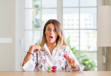 Genç kadın evde macarons sürpriz yüz işaret parmağı kendine yemek