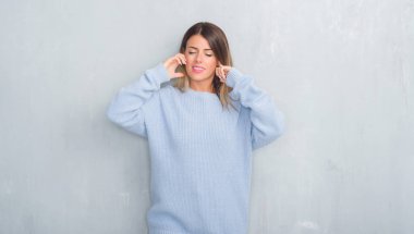 Yüksek sesle müzik gürültü rahatsız ifade parmaklarıyla kulaklarıyla kapsayan kış kıyafeti giymiş gri grunge duvarın üzerinden Genç Yetişkin kadın. Sağır kavramı.