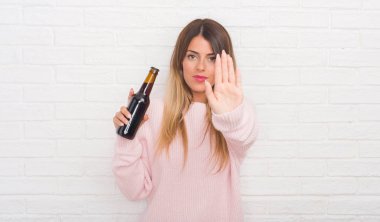 Bira ile holding beyaz tuğla duvarın üzerinden Yound yetişkin kadın dur işareti ile ciddi ve kendine güvenen ifade, savunma hareketi yaparken el açmak
