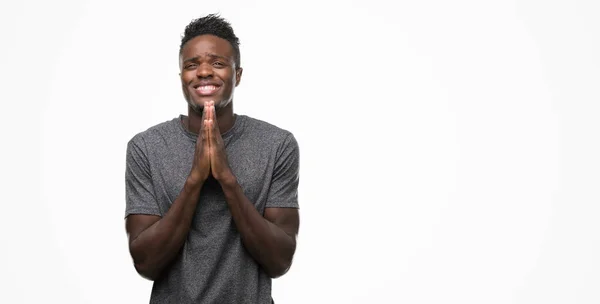 年轻的非洲裔美国男子身穿灰色 T恤祈祷双手一起请求原谅微笑自信 — 图库照片