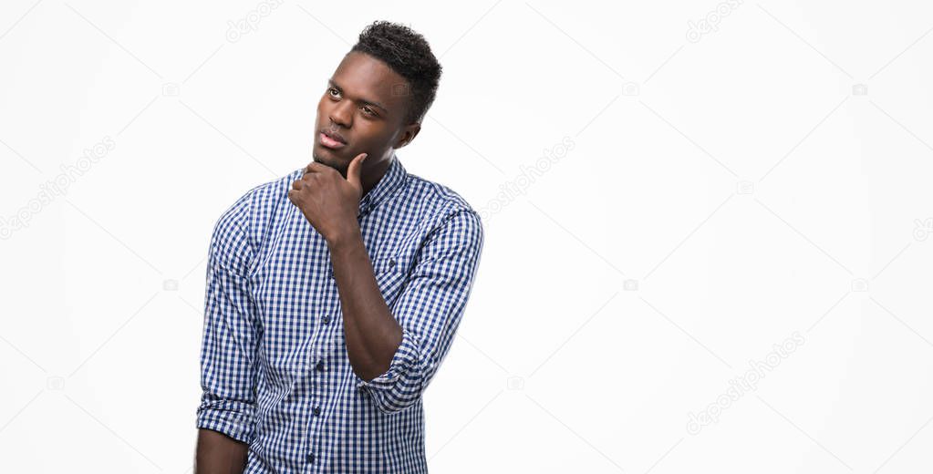 Young african american man wearing blue shirt with hand on chin thinking about question, pensive expression. Smiling with thoughtful face. Doubt concept.