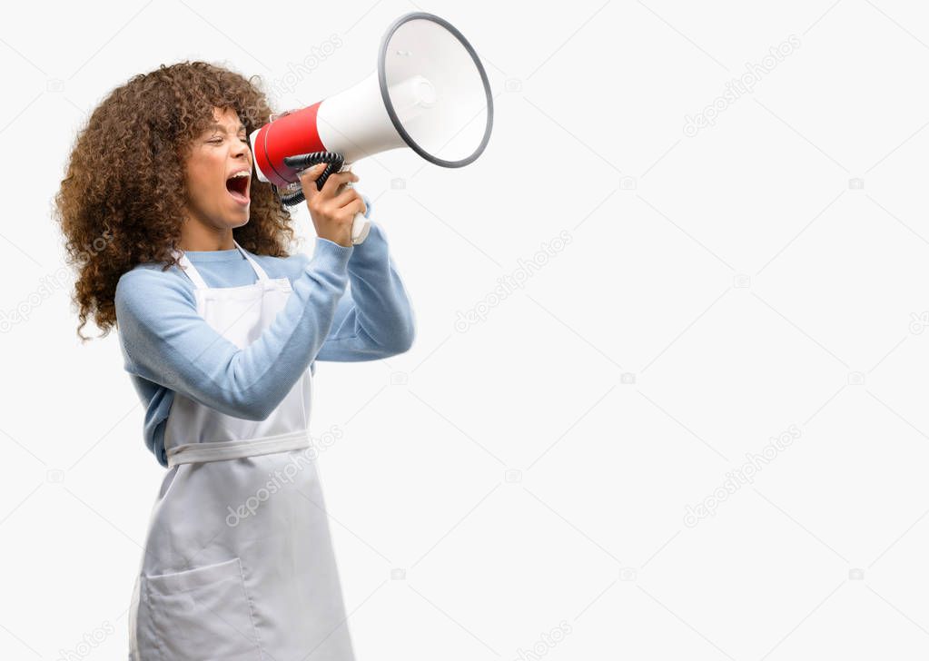 African american shop owner woman wearing an apron communicates shouting loud holding a megaphone, expressing success and positive concept, idea for marketing or sales