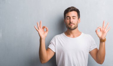 Yakışıklı genç gri grunge duvarın üzerinden rahatla ve gülümseyen gözlerle kapalı parmak jestle meditasyon yapıyor. Yoga kavramı.