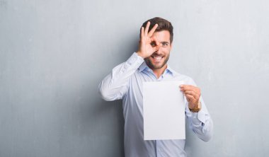 Boş kağıt sayfası sözleşme ile ok işareti ile el parmaklarının arasından seyir göze yapıyor gülümseyen mutlu yüz tutan gri grunge duvarın üzerinden yakışıklı genç