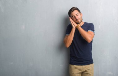 Uyku yorgun hayal ve eller ile birlikte kapalı gözlerle gülümseyerek poz gri grunge duvarın üzerinden yakışıklı genç.