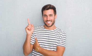 Kameraya bakarak yan el ve parmak ile işaret eden yakışıklı genç adam, yüzünde kocaman bir gülümseme ile Donanma t-shirt giyen gri grunge duvarın üzerinden.