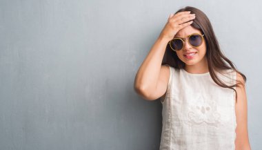 Genç esmer kadın baş, el ile vurguladı retro güneş gözlüğü takıyor grunge gri duvar yüzünden şok utanç ve sürpriz suratla, öfkeli ve sinirli. Korku ve hata için üzgün.