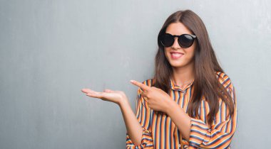 El ve parmak ile işaret çok mutlu büyük güneş gözlüğü takıyor grunge gri duvar genç esmer kadın