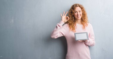 Parmak, mükemmel sembolü ile ok işareti yapıyor tablet kullanarak gri grunge duvar genç Kızıl saçlı kadın