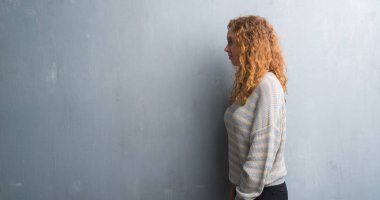 Genç Kızıl saçlı kadın tarafına, seyir gri grunge duvarın üzerinden dinlenmek doğal yüz emin gülümseme ile pozuyla profili.