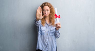 Genç redhead iş kadını elinde diploma ile gri grunge duvarın üzerinden açık el dur işareti ile ciddi ve kendine güvenen ifade, savunma hareketi yapıyor