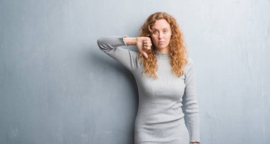 Genç Kızıl saçlı kadın kızgın yüz, gri grunge duvarın üzerinden negatif antipati başparmak aşağı, ret kavramı ile gösterilen işareti