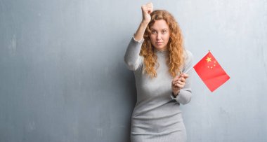Gri grunge duvar Çin rahatsız bayrağı ve öfke, çılgın ve yükseltilmiş el, öfke kavramı ile diye bağıran ile sinirli bağırarak tutan genç Kızıl saçlı kadın