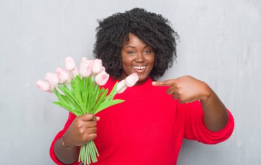 Pembe çiçekler Buket çok mutlu el ve parmak ile işaret tutan gri grunge duvarın üzerinden genç Afro-Amerikan kadın