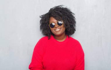 Genç Afro-Amerikan artı boyutu kadın yüzünde mutlu ve güzel bir gülümseme ile retro güneş gözlüğü takıyor gri grunge duvarın üzerinden. Şanslı kişi.