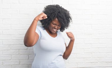 Çok mutlu ve heyecanlı kaldırdı kollarını açarak kazanan jest yapıyor, gülümseyen ve başarı için çığlık genç Afro-Amerikan artı boyutu kadın beyaz tuğla duvar. Kutlama kavramı.