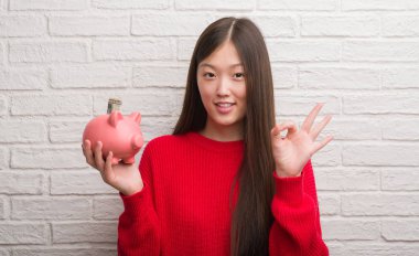 Kumbara parmak, mükemmel sembolü ile ok işareti yapıyor tutan tuğla duvarın üzerinden Genç Çinli kadın