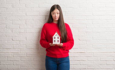 Genç Çinli gerçek durum Aracısı kadın acımak yüz ciddi düşünüyorum üstünde kendine güvenen bir ifade ile ev tutan tuğla duvarın üzerinden