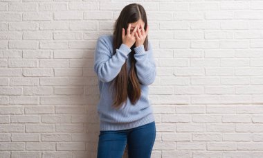 Genç Chinise kadın ağlayarak süre elleriyle yüzünü kapsayan üzgün ifade ile beyaz tuğla duvarın üzerinden. Depresyon kavramı.