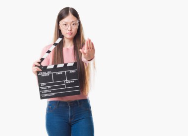 İzole arka plan holding clapper açık eliyle dur işareti ile ciddi ve kendine güvenen ifade, savunma hareketi yaparken Genç Çinli kadın