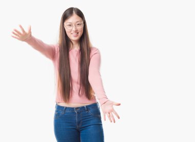 İzole arka plan sarılmak için kollarını açarak gülümseyerek kameraya bakarak gözlüklü Genç Çinli kadın. Neşeli ifade kucaklayan mutluluk.