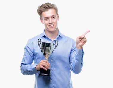 Genç yakışıklı sarışın adam bir kupa çok mutlu el ve parmak ile tarafına işaret tutan