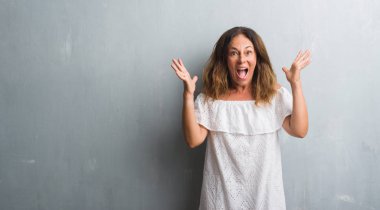 Üzerinde gri grunge duran orta yaş İspanyol kadın çılgın ve başarı için hayran kaldırdı kollarını açarak kutlama duvar ve heyecanlı çığlık gözleri açık. Kazanan kavramı