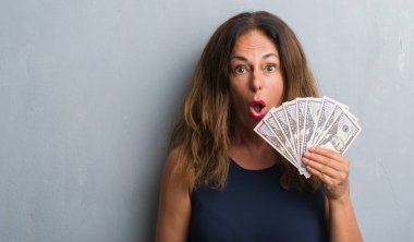 Dolar bir sürpriz yüz, korkuyor ve heyecanlı korku ifadesi ile şok korkmuş tutan gri grunge duvarın üzerinden duran orta yaş İspanyol kadın