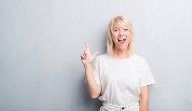 Grunge gri duvar işaret parmağı kadar başarılı fikri ile yetişkin beyaz kadın. Çıktıktan ve mutlu. Bir numara.