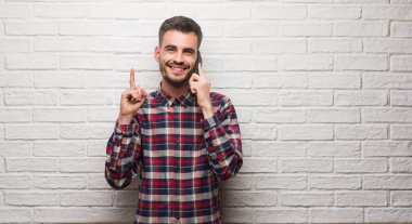 Genç Yetişkin üzerinde telefon duran beyaz tuğla duvarın üzerinden bir fikirle sürpriz konuşuyor dostum ya da gülen yüz, bir numara ile işaret parmağı soru