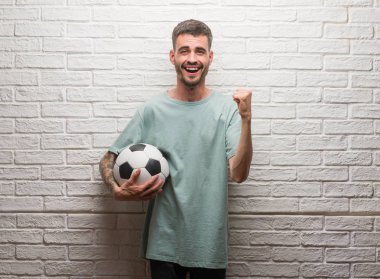Duygu tezahürat gurur çığlık ve zafer ve başarı çok heyecanlı, kutluyor beyaz tuğla duvarın üzerinden futbol topu ayakta tutan genç yetişkin adam