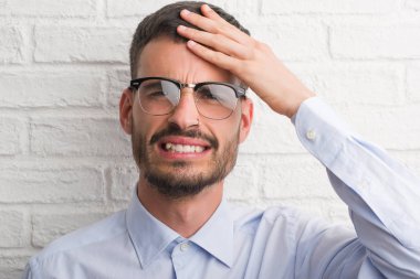 Genç Yetişkin iş adam kafasına, utanç ve sürpriz yüz ile şok el ile vurguladı beyaz tuğla duvarın üzerinden ayakta öfkeli ve sinirli. Korku ve hata için üzgün.